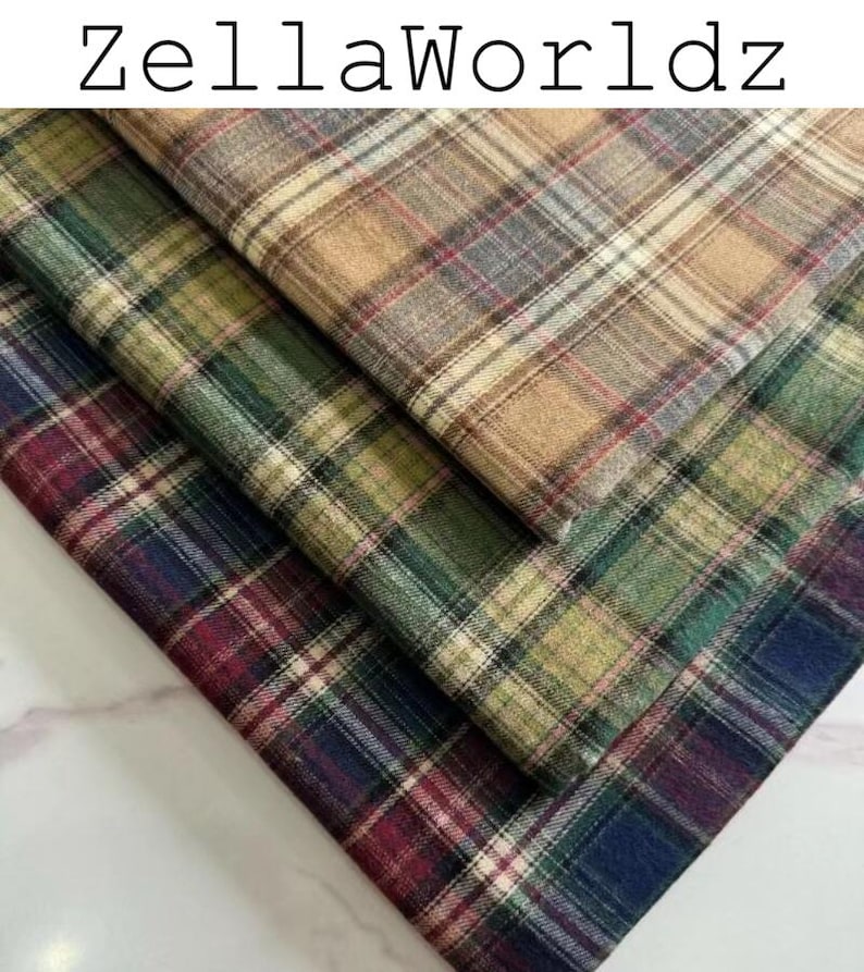 Pu&ograve; includere: Tre strati piegati di tessuto a quadri con il testo ZellaWorldz in alto. Lo strato superiore &egrave; color marrone chiaro, quello centrale &egrave; verde e quello inferiore &egrave; un mix di blu scuro, rosso e verde. Ogni strato mostra un classico motivo a linee.