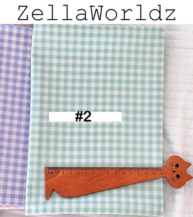 May include: Fabric samples with a gingham pattern in light green and purple. A wooden ruler with a cat design is placed on the green fabric. The text "ZellaWorldz" is at the top, and "#2" is on a white rectangle.