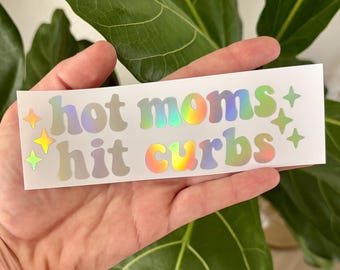 May include: A white sticker with iridescent rainbow lettering that reads "hot moms hit curbs" with small iridescent stars on either side of the text.