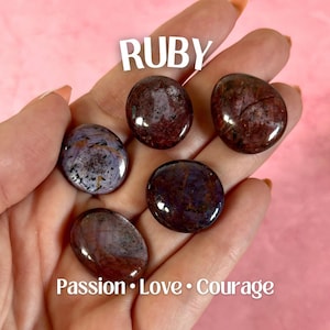 May include: Five polished ruby gemstones in varying shapes and sizes are displayed. The gemstones are primarily deep red with some purple and white marbling. The word "RUBY" is above the stones, and the words "Passion • Love • Courage" are below.