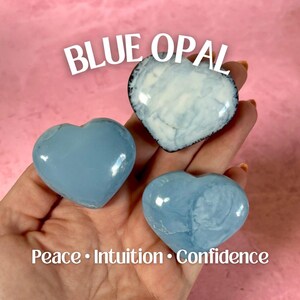 May include: Three blue opal heart-shaped stones are held in a hand against a pink background. The text "BLUE OPAL" is above the stones, and "Peace • Intuition • Confidence" is below.