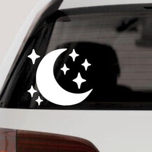 May include: White vinyl decal featuring a crescent moon and several four-pointed stars. The celestial design is applied to a car window, creating a decorative accent. The sticker is a simple, yet elegant, design for car enthusiasts.