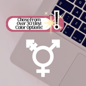 May include: A white transgender symbol sticker is displayed on a laptop. The image includes a pink and white banner with the text "Chose From Over 30 Vinyl Color Options!" and an exclamation point.