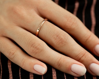 May include: A close-up of a hand wearing a thin gold band ring with the word "Grandma" engraved on it. The ring is on the ring finger of the left hand.