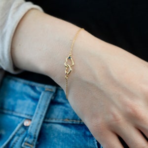 Op de afbeelding: Een gouden kettingarmband met twee in elkaar grijpende hartcharms. De harten hebben kleine blauwe en rode edelstenen.