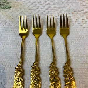 Könnte beinhalten: Set aus vier goldfarbenen Gabeln mit Rosen- und Blattmotiven. Die Gabeln sind aus Metall und haben eine polierte Oberfläche.