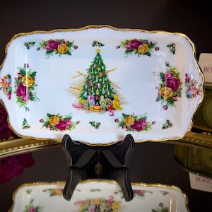 Puede incluir: Bandeja rectangular blanca con borde festoneado dorado, con diseño de árbol de Navidad y floral. La bandeja está decorada con un árbol de Navidad, regalos y rosas de colores. El logotipo de Royal Albert England es visible.