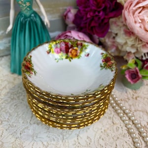 May include: A stack of eight white ceramic bowls with a gold rim and floral pattern. The bowls are stacked on a white lace tablecloth.