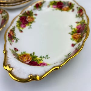 May include: A white oval serving dish with a gold rim and a floral pattern featuring red, yellow, and pink roses. The dish is made of fine china and has a delicate, scalloped edge.