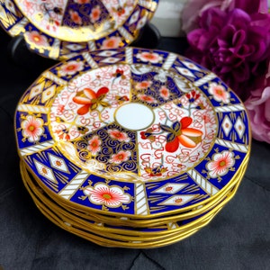 May include: A stack of fine china plates with a gold rim. The plates feature a white center with a floral design in red, orange, and blue. The outer edge of the plates is a deep blue with gold accents.