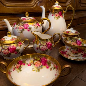 May include: A set of white porcelain teacups and teapot with gold trim and floral designs. The set includes a teapot, creamer, sugar bowl, teacup, and saucer.
