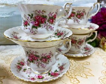 May include: Set of six vintage teacups and saucers with a floral pattern. The cups and saucers are white with a gold trim and feature pink roses and green leaves.