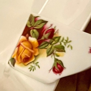 May include: A white ceramic serving dish with a floral design featuring yellow, red, and green roses. The dish is broken into two pieces.