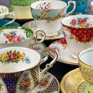 May include: A collection of vintage teacups and saucers with floral and gold designs. The cups are made of fine china and have delicate handles. The saucers are decorated with intricate patterns.