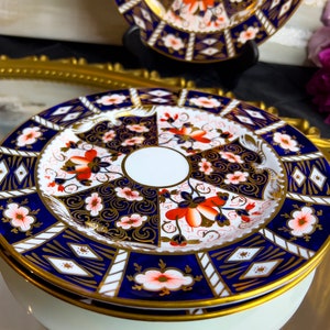 May include: A vintage porcelain teacup and saucer with a blue and gold floral pattern. The saucer has a white centre with a gold rim.