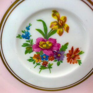 Puede incluir: Un platillo rosa con un borde dorado y un dise&ntilde;o floral en el centro. Las flores son amarillas, rosas, naranjas, azules y moradas.