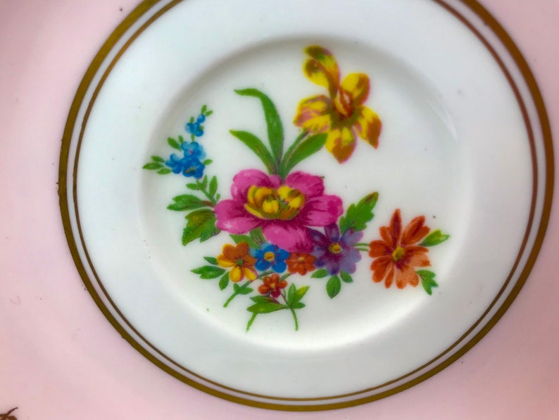 Puede incluir: Un platillo rosa con un borde dorado y un dise&ntilde;o floral en el centro. Las flores son amarillas, rosas, naranjas, azules y moradas.