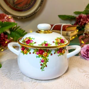 Puede incluir: Olla de esmalte blanco con un diseño floral con rosas rojas, amarillas y rosas. La olla tiene un borde dorado y una perilla dorada en la tapa.