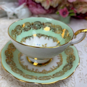 May include: A mint green teacup and saucer set with gold filigree detailing. The teacup has a rounded shape with a gold handle and rim. The saucer mirrors the cup's design, creating a cohesive and elegant aesthetic. A classic tea set.