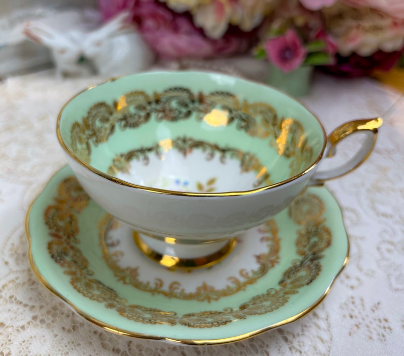 May include: A mint green teacup and saucer set with gold filigree detailing. The teacup has a rounded shape with a gold handle and rim. The saucer mirrors the cup's design, creating a cohesive and elegant aesthetic. A classic tea set.