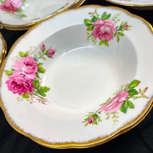 May include: A set of four white ceramic soup bowls with a gold rim and a pink rose floral pattern.