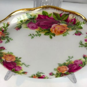 May include: A white porcelain saucer with a gold rim and a floral design featuring pink, yellow, and red roses. The saucer is perfect for teacups or other small dishes.