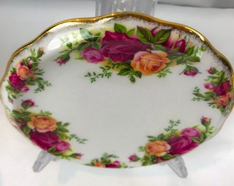 May include: A white porcelain saucer with a gold rim and a floral design featuring pink, yellow, and red roses. The saucer is perfect for teacups or other small dishes.