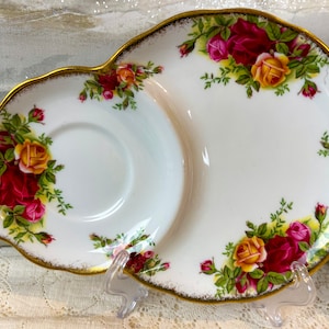 May include: A white porcelain teacup and saucer set with a gold rim and floral design. The saucer has a divided section for snacks or a sandwich.