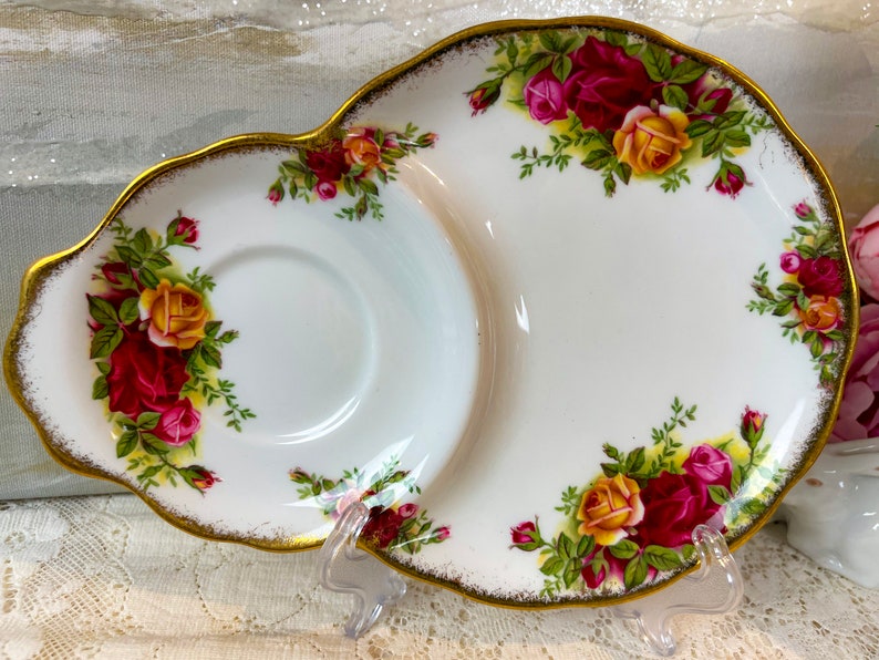 May include: A white porcelain teacup and saucer set with a gold rim and floral design. The saucer has a divided section for snacks or a sandwich.