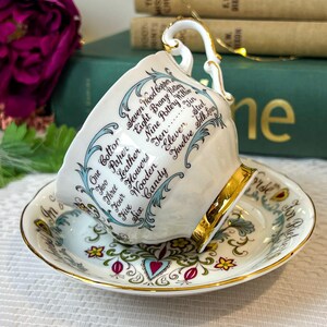 May include: A white teacup and saucer with a gold trim. The teacup has a blue and white floral design and the words "One Cotton, Two Paper, Three Leather, Four Flowers, Five Wooden, Six Candy, Seven Wood Copper, Eight Bronze Pottery, Nine Pottery Willow, Ten Jin, Eleven Steel, Twelve Silk Linen" written around the side. The saucer has a similar floral design with a gold trim.