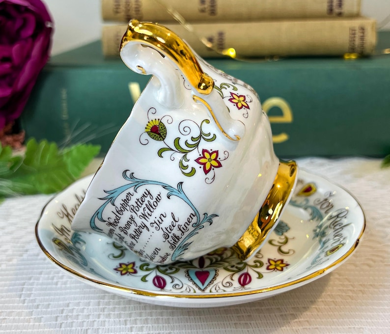 May include: A white teacup and saucer with a gold rim and floral pattern. The teacup has a gold handle and the saucer has the text "For All Occasions" written on it. The teacup has the text "Wood Copper, Bronze Pottery, Willow, Jin, Steel, Silk Linen" written on it.