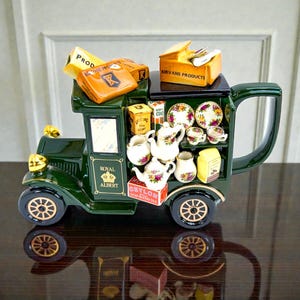 May include: A decorative ceramic tea set in the shape of a vintage truck. The dark green truck features gold accents, a large handle, and is filled with miniature teacups, teapots, and boxes of tea. The Royal Albert logo is visible on the side.