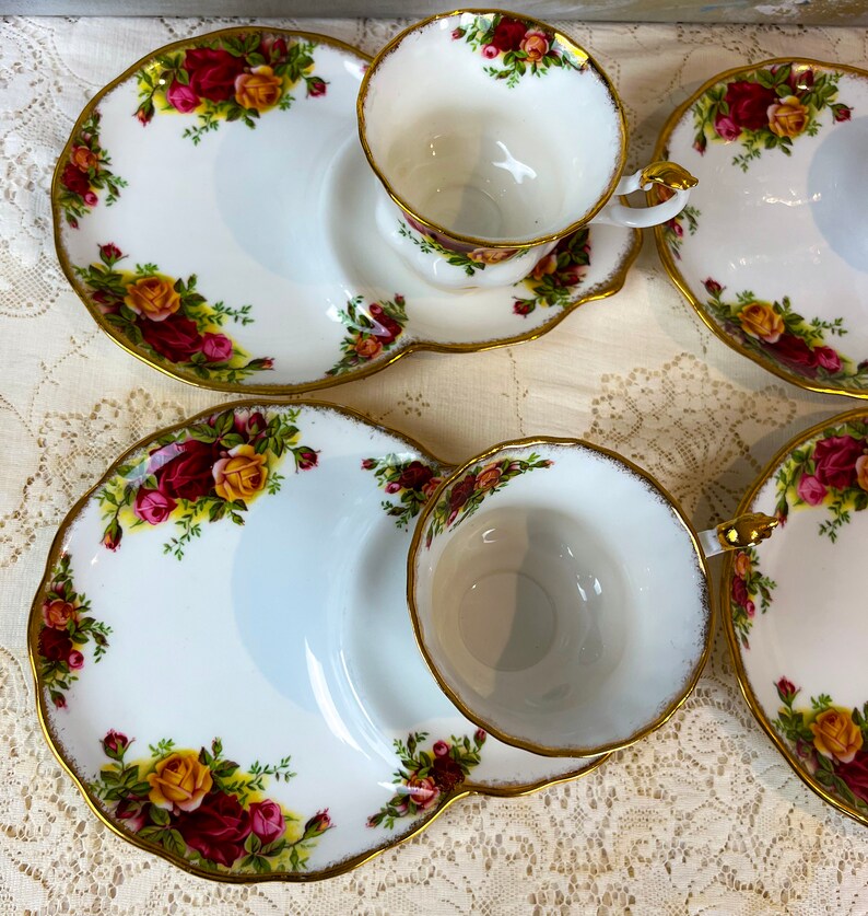 May include: A set of three white teacups and saucers with a gold rim and floral pattern. The saucers have a small side plate for snacks.