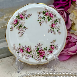 May include: A white porcelain teacup saucer with a gold rim and a floral pattern of pink roses and green leaves.
