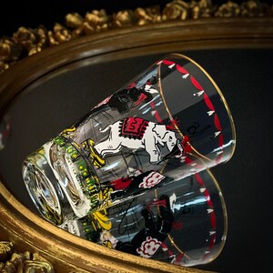May include: A clear glass tumbler with a circus theme. The tumbler features a black and white illustration of elephants, clowns, and other circus performers. The tumbler has a red and white striped band around the top.