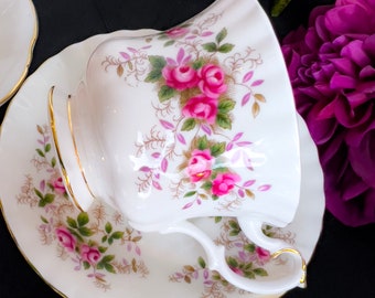 May include: A white teacup and saucer with a floral pattern of pink roses and green leaves. The cup and saucer have a gold trim.