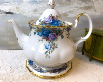 May include: A white teapot with a blue and purple floral pattern. The teapot has a gold trim and a matching saucer.