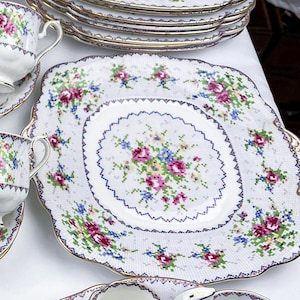 Peut inclure: Un ensemble de tasses et soucoupes à thé en porcelaine blanche avec un motif floral délicat. Les tasses et les soucoupes ont un bord festonné et une bordure dorée. L'ensemble comprend un plat de service carré avec un motif floral similaire.