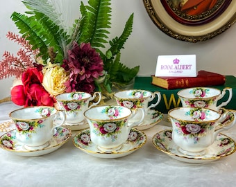 May include: Set of six Royal Albert teacups and saucers with a floral pattern featuring pink, white, and green roses. The cups and saucers have a gold trim.