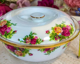 May include: White ceramic serving bowl with lid, featuring a floral rose pattern in shades of pink, yellow, and green. The bowl has a gold rim and a small gold knob on the lid. The bowl measures approximately 4 inches in height.