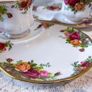 May include: A white porcelain teacup and saucer set with a gold rim and floral pattern. The saucer has a scalloped edge and a small plate attached to it.