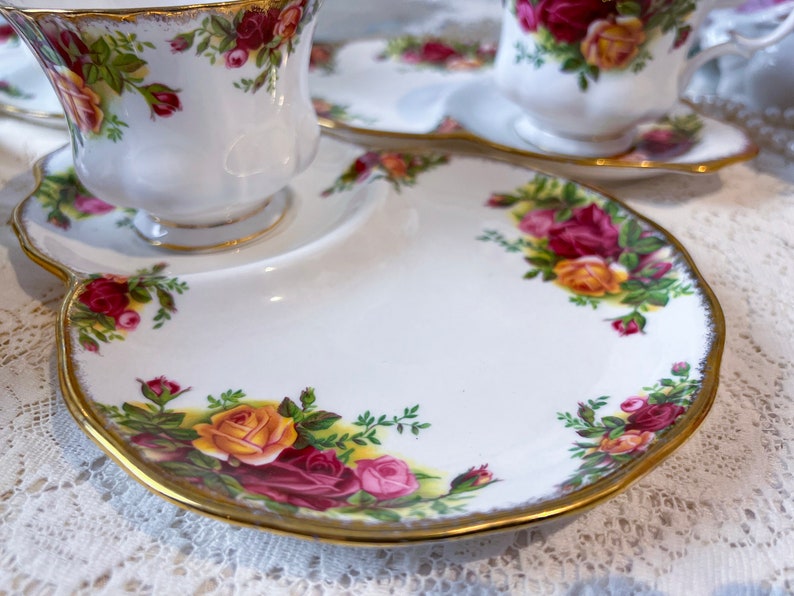 May include: A white porcelain teacup and saucer set with a gold rim and floral pattern. The saucer has a scalloped edge and a small plate attached to it.