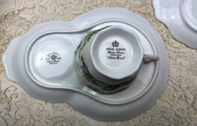 May include: A white Royal Albert Silver Birch bone china teacup and saucer set. The teacup is placed on a matching tray with a floral design. The set includes the text "Royal Albert Bone China England Silver Birch".
