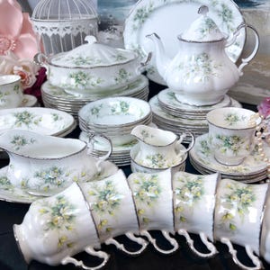 May include: A set of white fine china dinnerware with a floral pattern in shades of green and yellow. The set includes plates, bowls, cups, saucers, a teapot, a gravy boat, and a creamer.