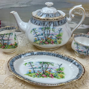 May include: A white tea set with a birch tree design. The set includes a teapot, creamer, sugar bowl, and a serving plate. The set has a grey and gold trim.