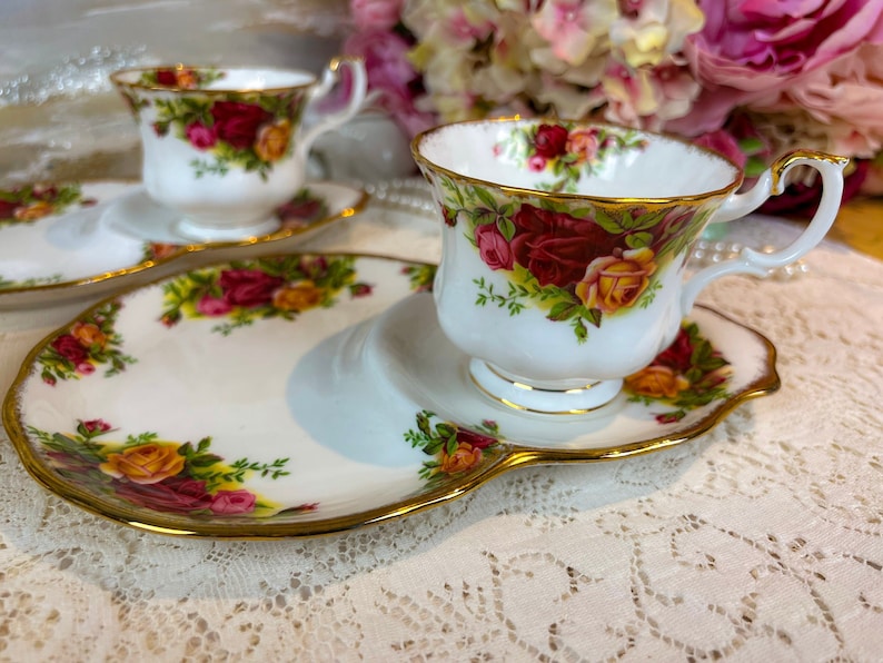 May include: Two white teacups and saucers with a floral pattern. The saucers are decorated with a gold trim. The teacups are filled with tea.