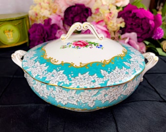 May include: A turquoise and white porcelain serving dish with a gold trim and floral design. The dish has a lid with a floral design and a gold handle.