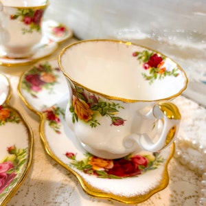May include: A white teacup and saucer with a floral pattern and gold trim. The teacup has a delicate handle and the saucer has a scalloped edge.