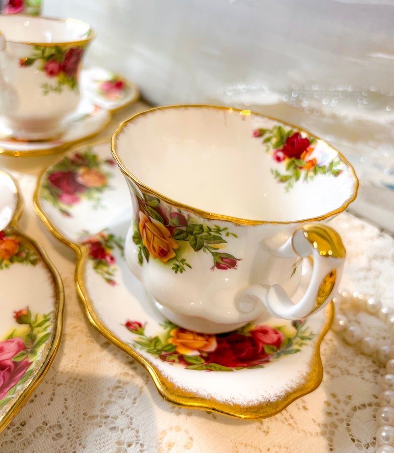 May include: A white teacup and saucer with a floral pattern and gold trim. The teacup has a delicate handle and the saucer has a scalloped edge.