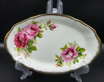 May include: A white oval serving dish with a gold rim and a pink rose floral pattern.